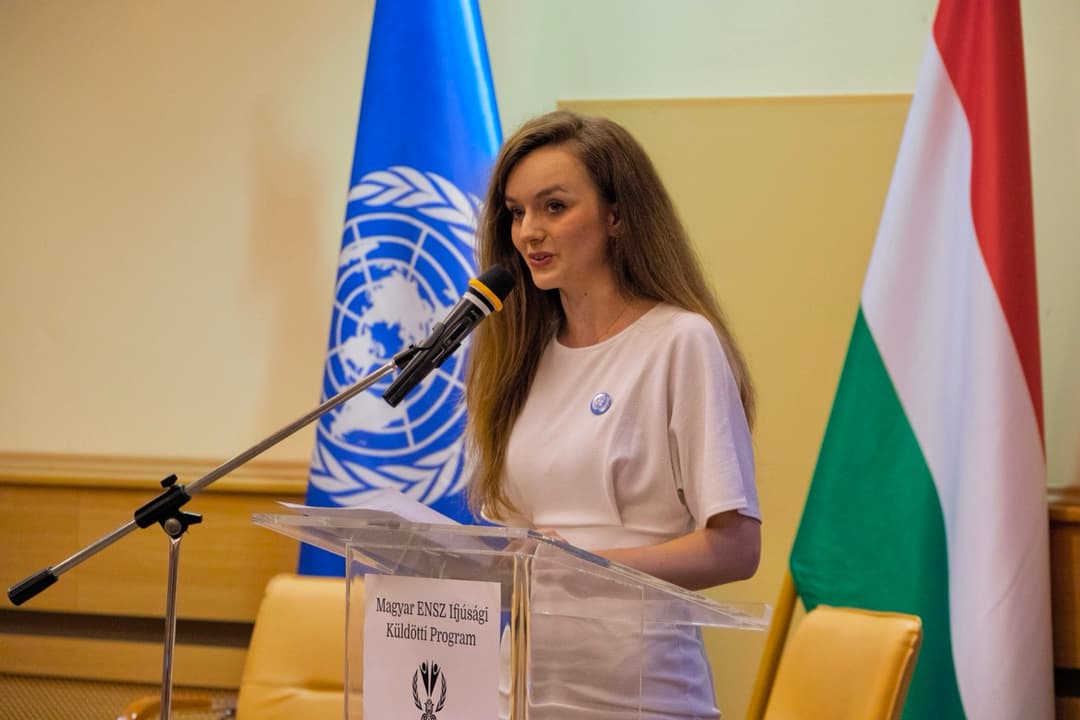 Annamaria speaking at a podium between the UN and Hungarian flags